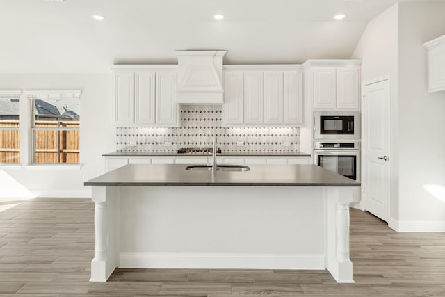 kitchen with backsplash, oven, black microwave, and white cabinets