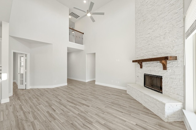 unfurnished living room featuring a fireplace, light hardwood / wood-style floors, ceiling fan, and a high ceiling