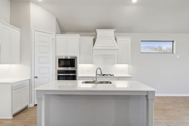 kitchen with built in microwave, white cabinetry, an island with sink, and stainless steel oven