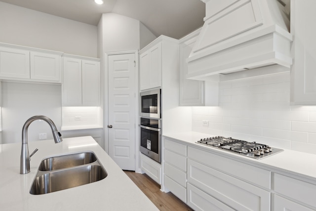 kitchen featuring appliances with stainless steel finishes, white cabinetry, sink, backsplash, and custom range hood