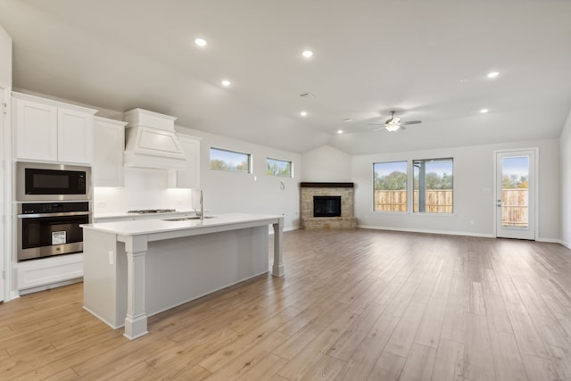 kitchen featuring sink, white cabinetry, an island with sink, built in microwave, and stainless steel oven