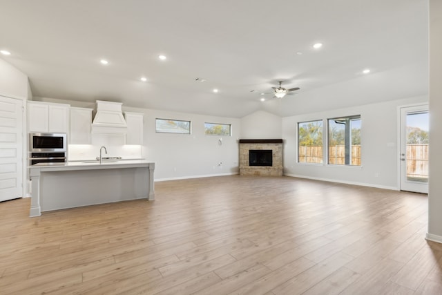 unfurnished living room with ceiling fan, a stone fireplace, vaulted ceiling, and light hardwood / wood-style flooring