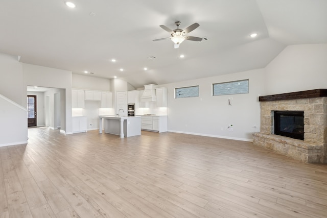 unfurnished living room with lofted ceiling, sink, light wood-type flooring, ceiling fan, and a fireplace