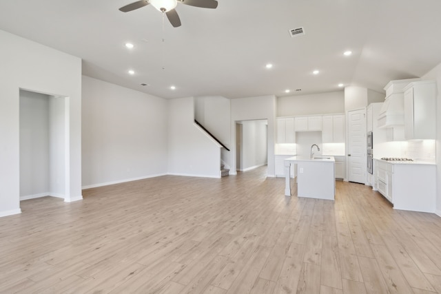 unfurnished living room with sink, light hardwood / wood-style floors, and ceiling fan