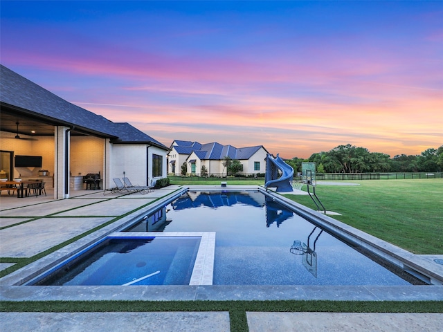 pool at dusk with a water slide and a yard