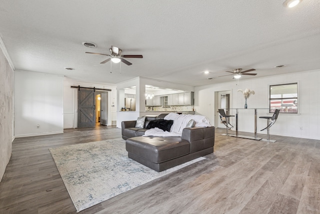 living room featuring hardwood / wood-style flooring, a textured ceiling, ceiling fan, a barn door, and crown molding