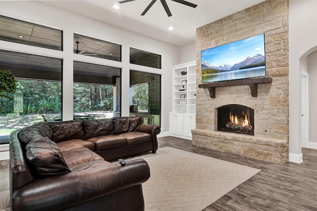 living area with arched walkways, ceiling fan, a fireplace, wood finished floors, and baseboards