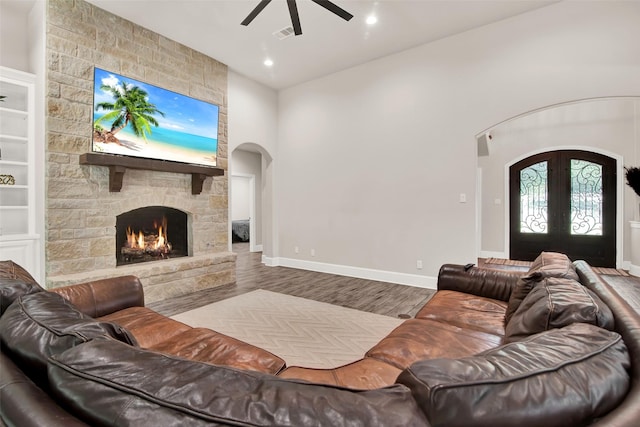 living area with baseboards, arched walkways, wood finished floors, french doors, and a fireplace