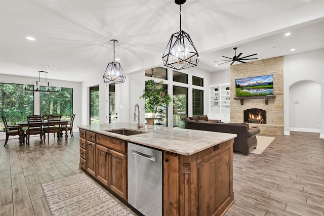 kitchen featuring light stone counters, wood finish floors, a sink, stainless steel dishwasher, and an island with sink