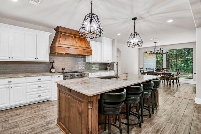 kitchen featuring arched walkways, a sink, high end stainless steel range, light stone countertops, and custom range hood