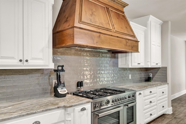 kitchen featuring range with two ovens, white cabinets, custom exhaust hood, and light stone countertops