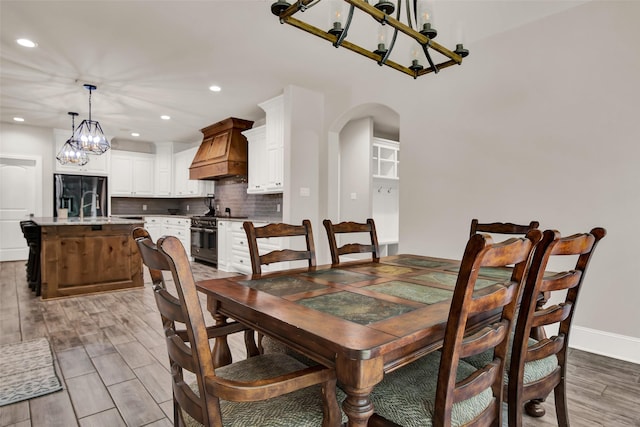 dining room with arched walkways, recessed lighting, baseboards, light wood finished floors, and an inviting chandelier