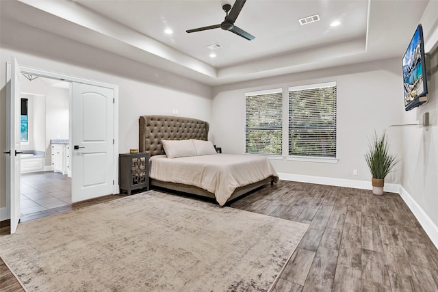 bedroom featuring wood finished floors, a raised ceiling, visible vents, and baseboards