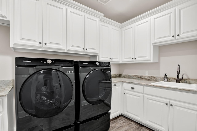 washroom featuring cabinet space, visible vents, washer and dryer, light wood-type flooring, and a sink