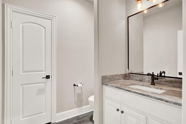 bathroom featuring toilet, baseboards, wood finished floors, and vanity