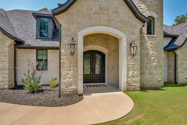 entrance to property with stone siding, french doors, roof with shingles, and brick siding