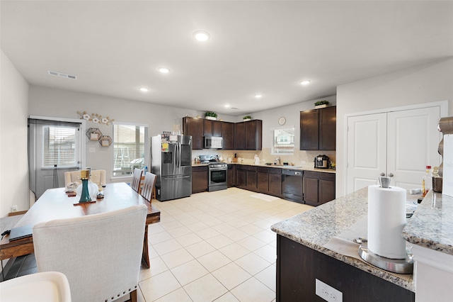 kitchen with stainless steel appliances, sink, dark brown cabinetry, light stone countertops, and light tile patterned flooring