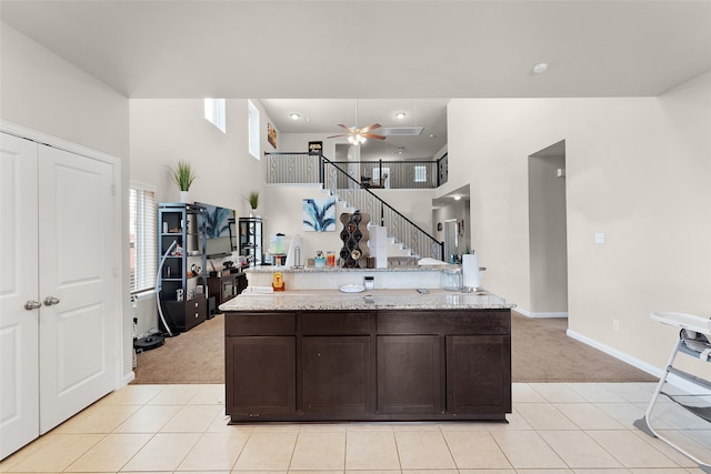 kitchen with dark brown cabinets, light stone countertops, ceiling fan, and light tile patterned floors