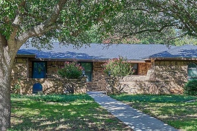 single story home with brick siding, a front yard, and a shingled roof