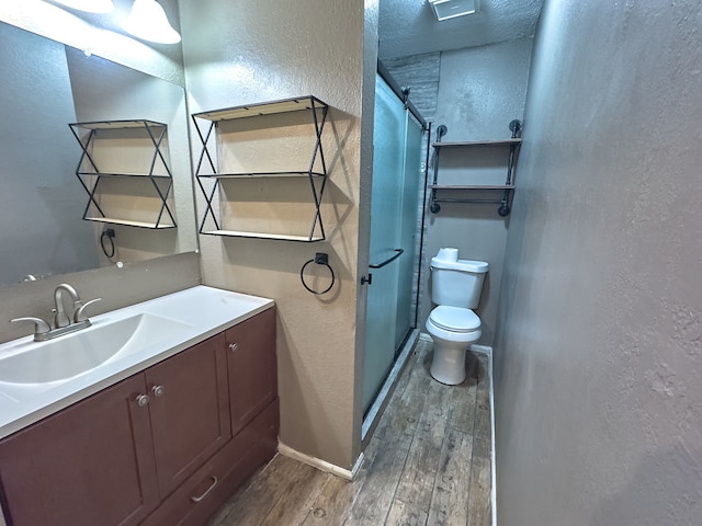 bathroom with toilet, a shower with shower door, hardwood / wood-style floors, and vanity