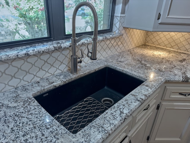 interior details with sink, decorative backsplash, light stone counters, and white cabinets