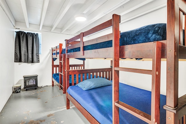 bedroom with concrete floors, a wood stove, and beamed ceiling