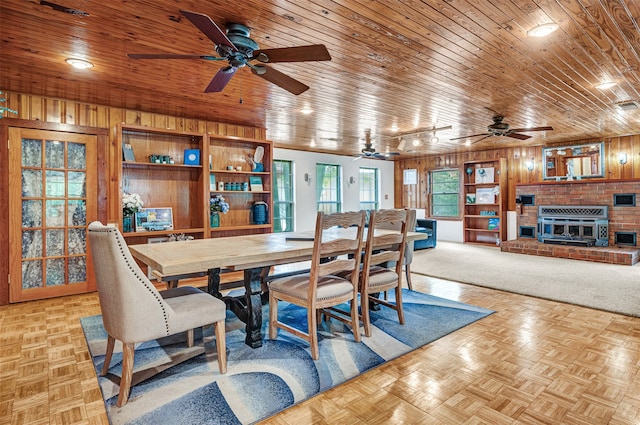 dining area with wood ceiling, a fireplace, light parquet floors, wood walls, and ceiling fan