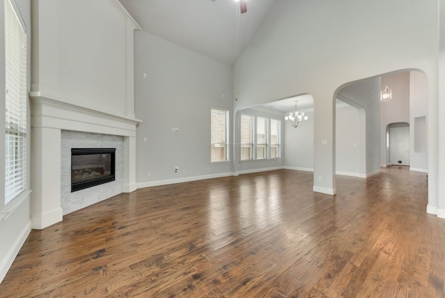 unfurnished living room with high vaulted ceiling, ceiling fan with notable chandelier, and dark hardwood / wood-style flooring