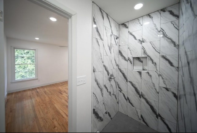 bathroom with a tile shower and wood-type flooring