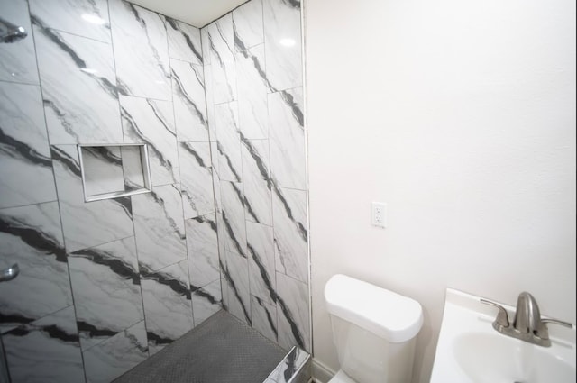 bathroom featuring tiled shower, sink, and toilet