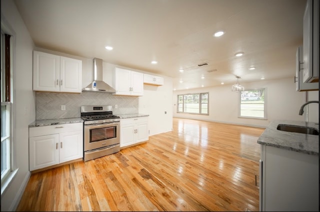 kitchen featuring white cabinets, wall chimney range hood, sink, gas stove, and light hardwood / wood-style floors