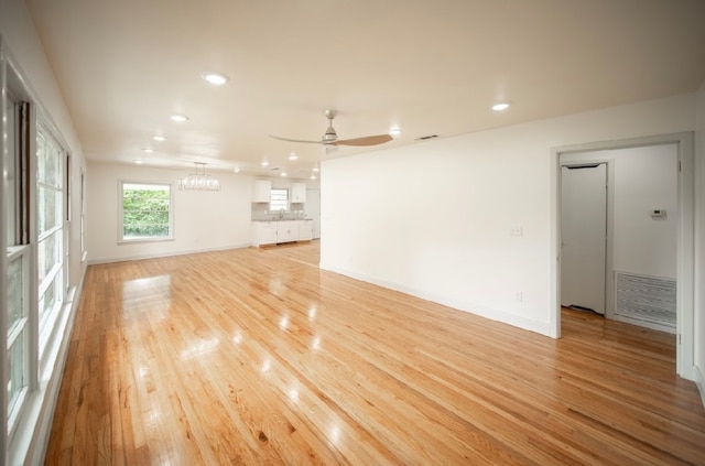 unfurnished living room with sink, ceiling fan with notable chandelier, and light hardwood / wood-style floors