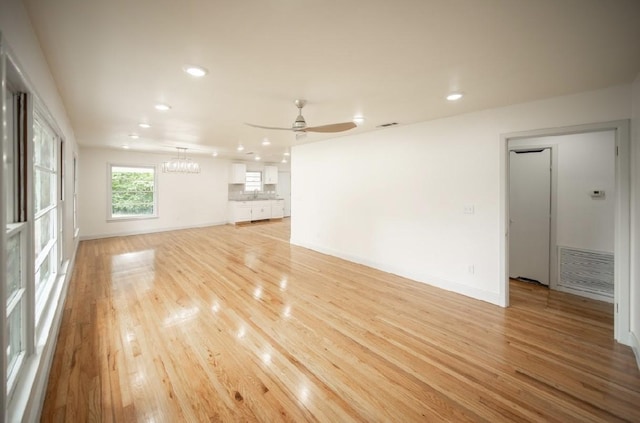 unfurnished living room featuring sink, ceiling fan with notable chandelier, and light hardwood / wood-style floors