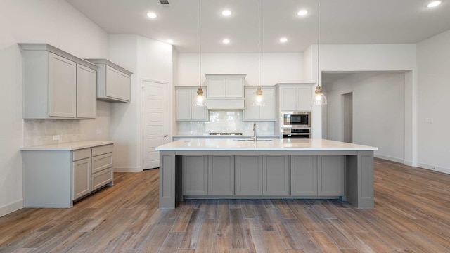 kitchen featuring gray cabinets, a kitchen island with sink, pendant lighting, dark wood-type flooring, and stainless steel appliances