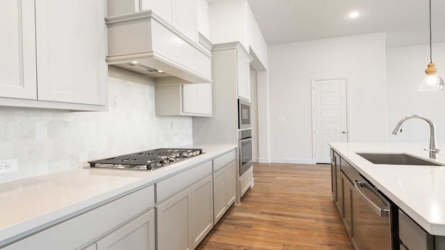 kitchen with premium range hood, sink, light hardwood / wood-style flooring, appliances with stainless steel finishes, and decorative light fixtures