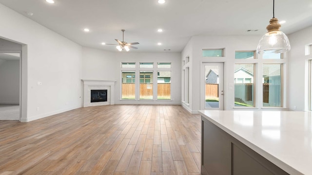 unfurnished living room featuring ceiling fan, light wood-type flooring, and a wealth of natural light