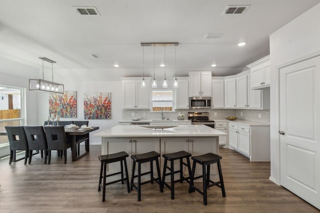 kitchen with white cabinets, appliances with stainless steel finishes, hanging light fixtures, and a center island