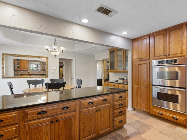 kitchen with dark stone counters, stainless steel double oven, a chandelier, and a textured ceiling