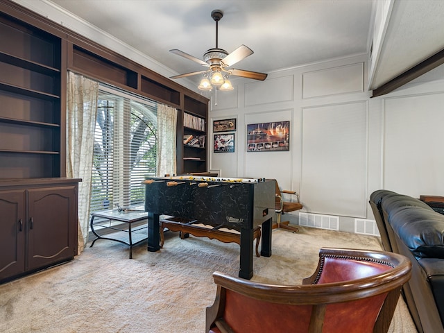 game room with crown molding, built in shelves, ceiling fan, and light colored carpet