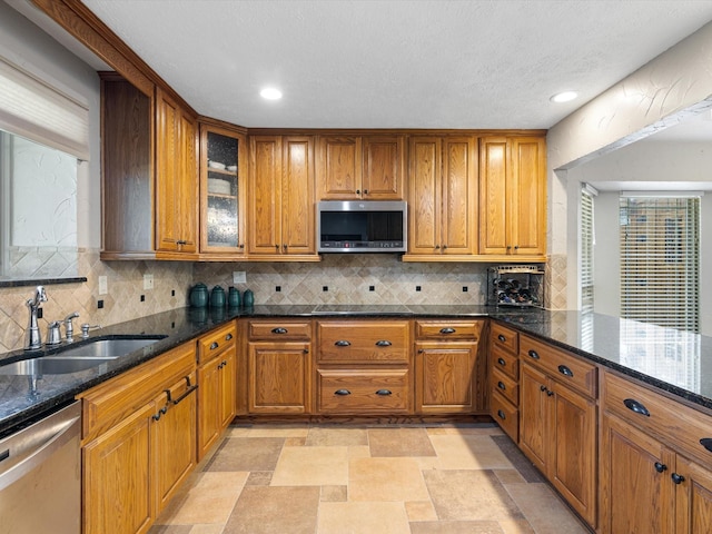 kitchen with appliances with stainless steel finishes, dark stone counters, sink, light tile patterned floors, and decorative backsplash