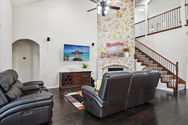 living room with a towering ceiling, a stone fireplace, dark wood-type flooring, and ceiling fan