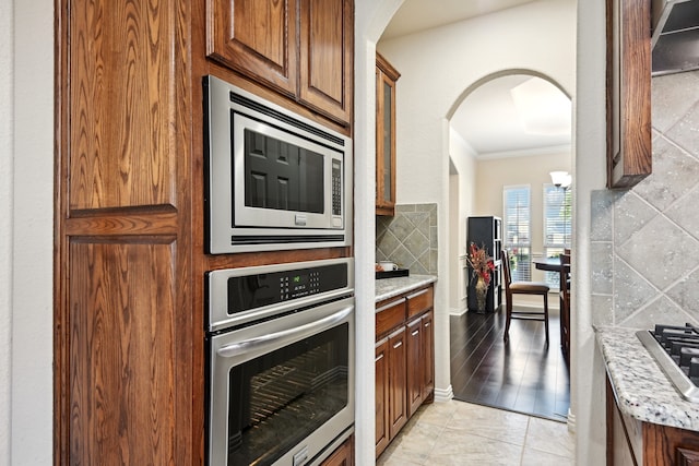 kitchen featuring appliances with stainless steel finishes, light hardwood / wood-style floors, light stone countertops, ornamental molding, and decorative backsplash