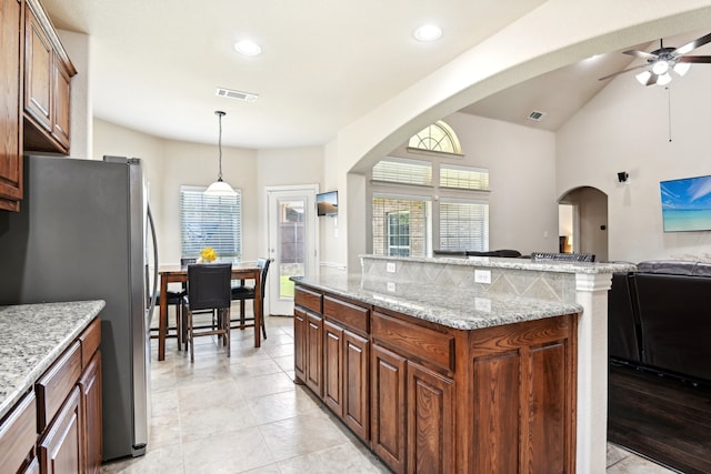 kitchen featuring ceiling fan, light stone counters, light tile patterned floors, and stainless steel refrigerator