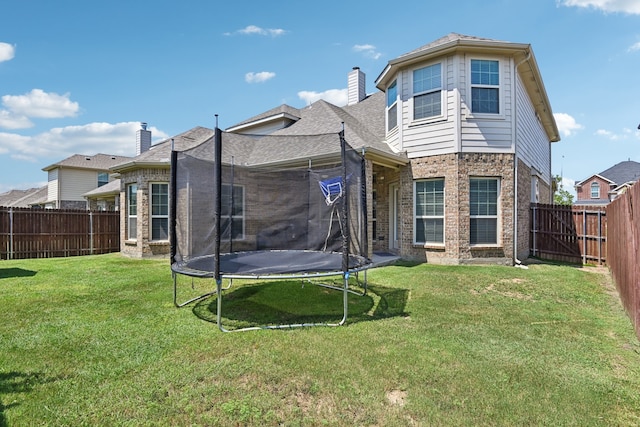 rear view of house featuring a trampoline and a lawn