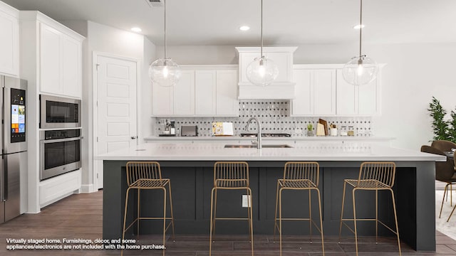 kitchen with white cabinetry, pendant lighting, appliances with stainless steel finishes, and an island with sink