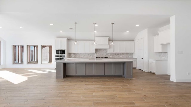 kitchen featuring white cabinetry, decorative light fixtures, a kitchen island with sink, and tasteful backsplash