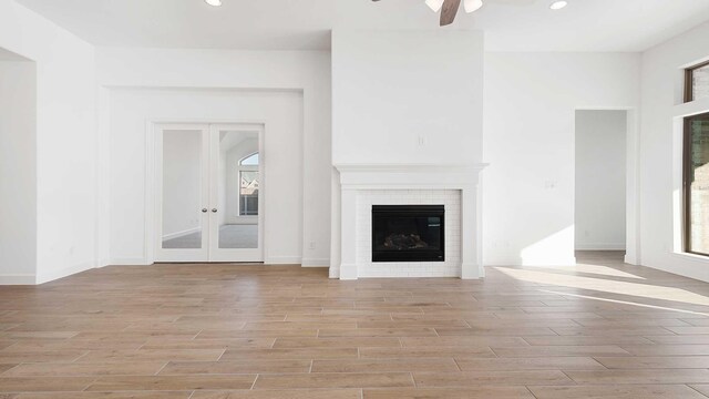 unfurnished living room featuring a fireplace, light hardwood / wood-style floors, french doors, and ceiling fan