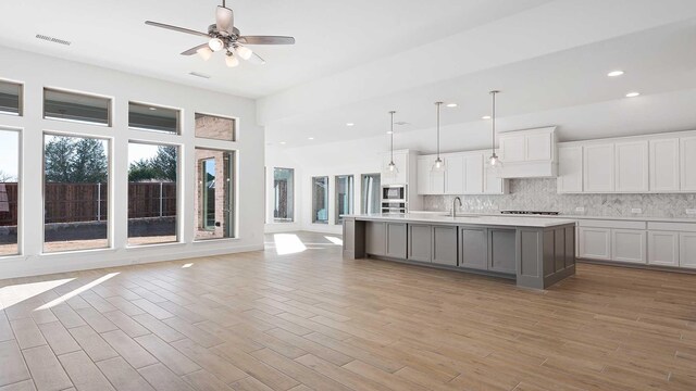 kitchen featuring tasteful backsplash, light hardwood / wood-style floors, a kitchen island with sink, and hanging light fixtures