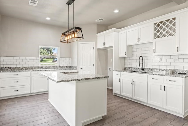 kitchen with sink, pendant lighting, backsplash, a kitchen island, and white cabinetry