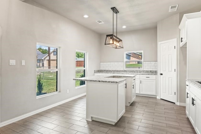 kitchen featuring white cabinetry, light stone countertops, hanging light fixtures, and tasteful backsplash